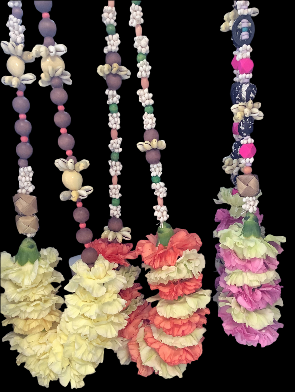 Three lei with carnations and beads and shells on a black back ground