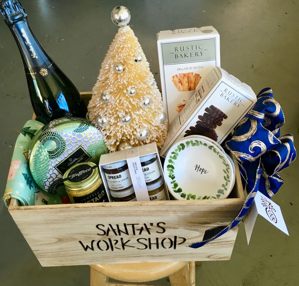 Gift box showing champagne, candle, crackers, cookies, tea towel,set of dipping dishes, set of spreads, truffle mustard and small table top Christmas tree.