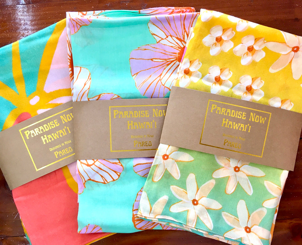 3 gorgeous Hawaiian pareos folded in package on a table fanned out