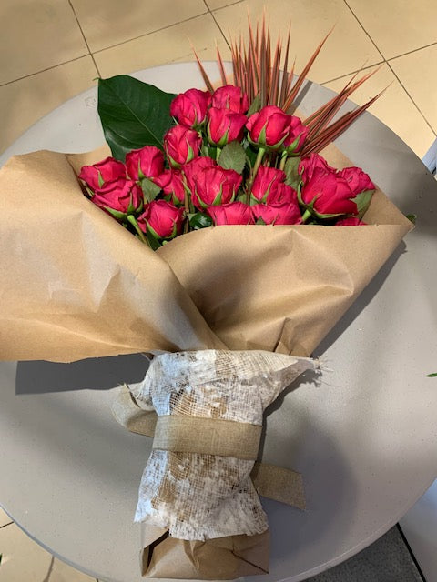bundle of pink roses with large leaves ties with paper
