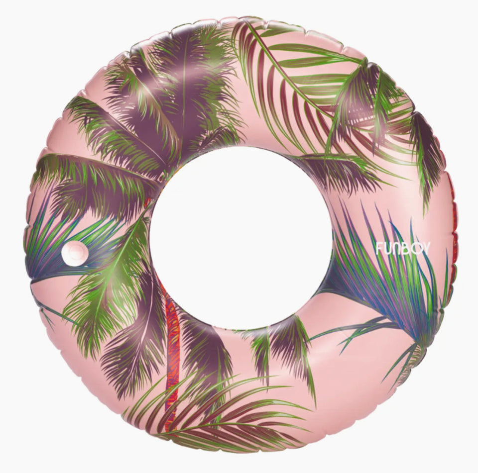 Inner tube out of package green palm leaves on a pink background