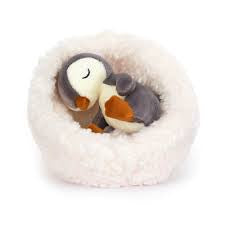 stuffed penquin sleeping in white fluffy bed