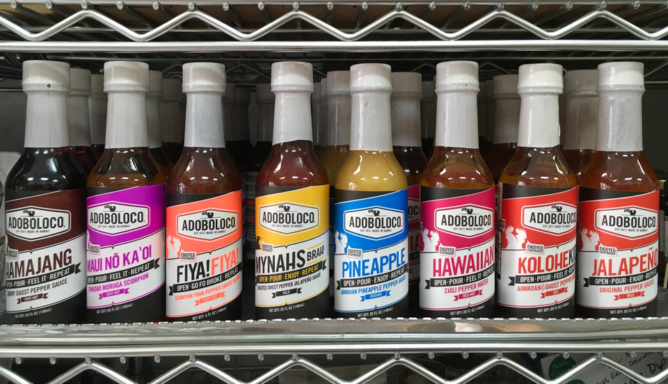 Shelf display of all the flavors of hot sauce. lined up Hamajang, Maui No Ka Oi, Fiya Fiya, Mynahs, Hawaiian, Kolohekid, Jalapeno