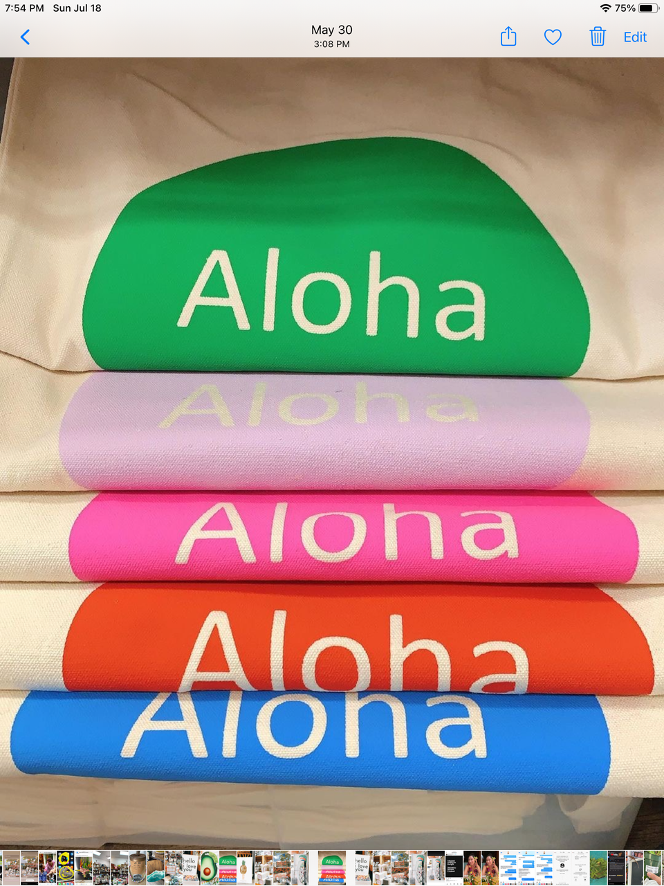 folded totes on shelf all different colors they all say aloha in the center. blue and orange pink lavender and green options.