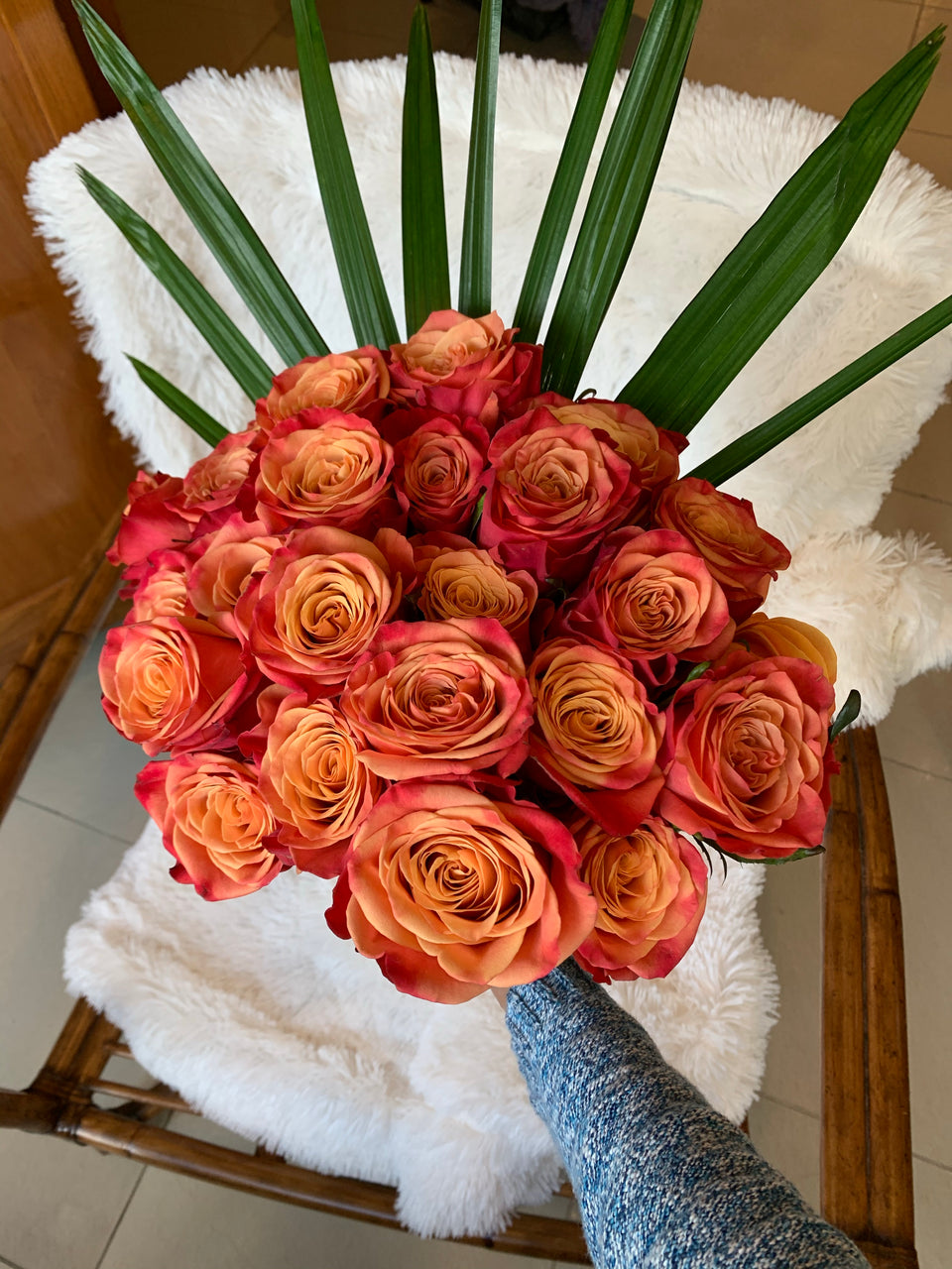 Hand holding orange roses with large green leaves