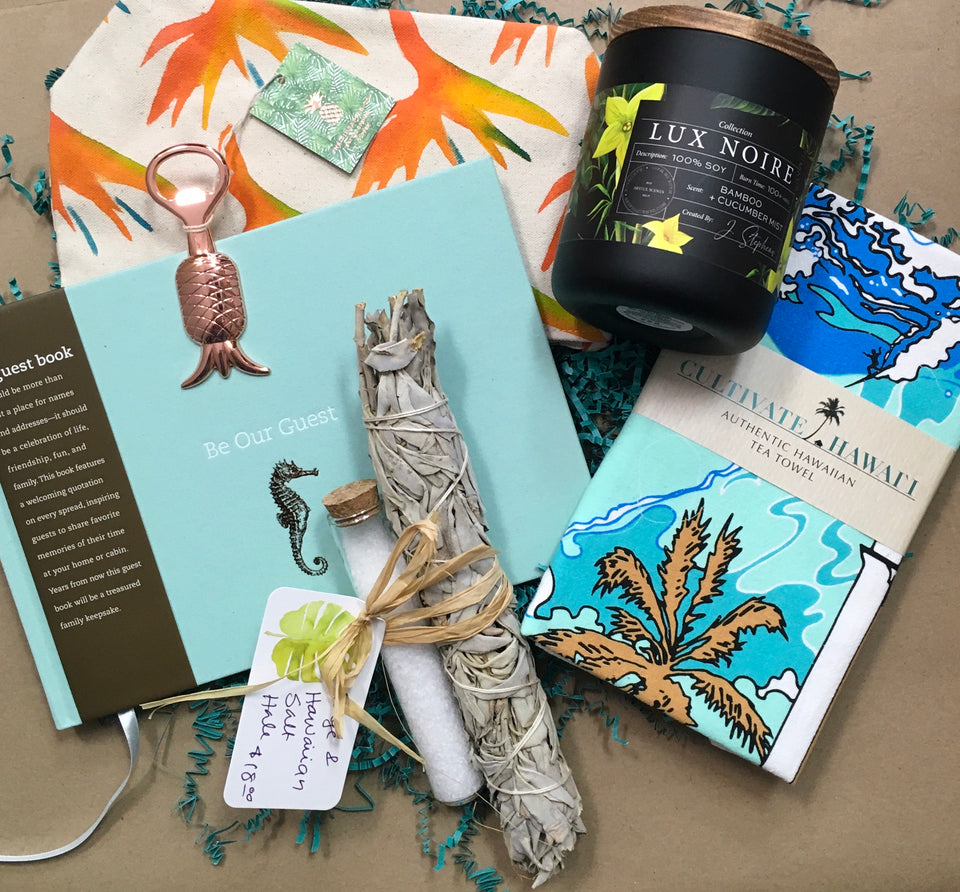 close up of housewarming basket. Large candle, dishtowel, guest book, pineapple bottle opener, sage, hawaiian sea salt