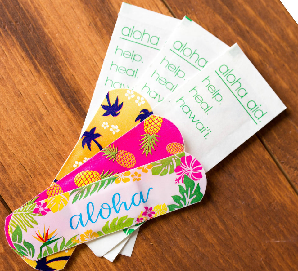 Aloha aid bandaids are printed with the word aloha and pineaples and palm trees - photo of the three designs and the outside wrappers that say aloha aid. help. heal. hawaii.